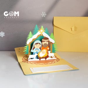 Pu&ograve; includere: Un biglietto di Natale pop-up giallo raffigurante la scena della nativit&agrave;. Il biglietto presenta un design dettagliato in carta ritagliata di Maria, Giuseppe, Ges&ugrave; bambino, alberi, una stella e pecore. Il biglietto ha il testo "GOM Art Craft".