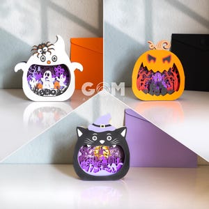 Könnte beinhalten: Drei Halloween-Themen-Papier-Ausschnitte. Ein weißer Geist mit einer Spinne, ein orangefarbener Kürbis und eine schwarze Katze mit Hexenhut. Jeder Ausschnitt hat eine detaillierte Innenszene mit lila und orangefarbenen Akzenten.