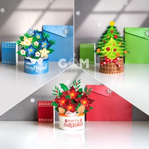May include: Three festive paper art arrangements for Christmas. One displays blue and white flowers, another a green Christmas tree, and the last, red poinsettias. Each is in a decorative container with the words "Merry Christmas".