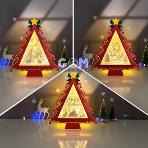 Può includere: Tre decorazioni luminose ad albero di Natale rosse e bianche con scene diverse all'interno. Il primo albero ha una scena della natività, il secondo ha una scena invernale con un cervo, e il terzo ha un messaggio 'Buon Natale' con un gatto e un cane.
