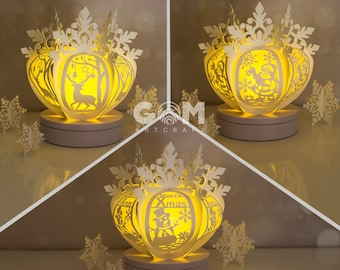 May include: Three white paper snowflake light-up ornaments with different Christmas scenes. The first ornament features a deer in a forest, the second features a snowman, and the third features a Santa Claus figure.