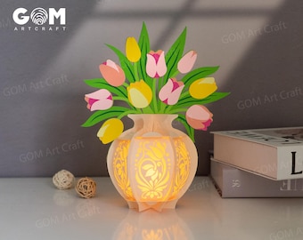 Könnte beinhalten: Eine 3D-Pop-up-Karte aus Papier mit einer Vase mit einem Strauß rosa und gelber Tulpen. Die Vase ist aufwendig mit einem Blumenmuster verziert und von innen beleuchtet, wodurch ein warmes Leuchten entsteht.