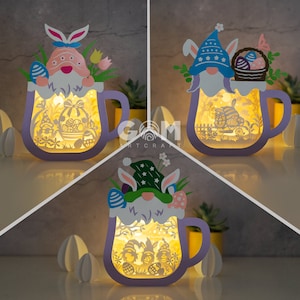 May include: Three purple ceramic mugs with bunny and gnome designs. Each mug has a light inside and is decorated with Easter eggs and flowers.