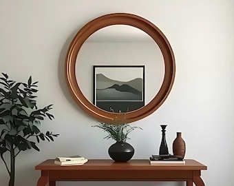 May include: A circular, wooden-framed mirror is mounted above a brown console table. The table displays a black vase with greenery, decorative bottles, and books. A potted plant is to the left. The mirror reflects a framed landscape painting.