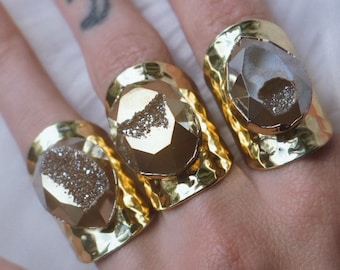 May include: Three gold rings with large, faceted, clear quartz stones. The stones have a sparkly, glittery texture.