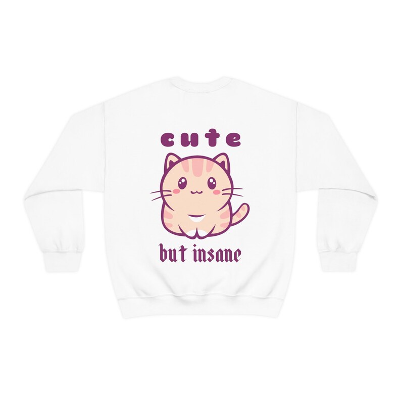 Może przedstawiać: Biała bluza z kresk&oacute;wkowym kotem i napisem "cute but insane" w kolorze fioletowym.