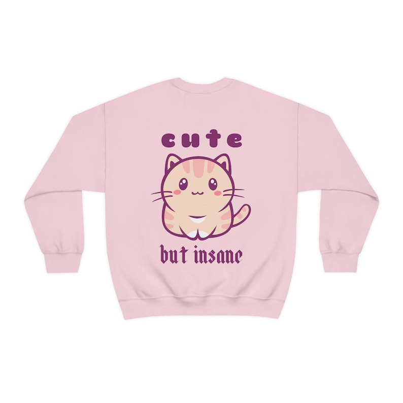 Może przedstawiać: R&oacute;żowa bluza z kresk&oacute;wkowym kotem i napisem "cute but insane" w kolorze fioletowym.