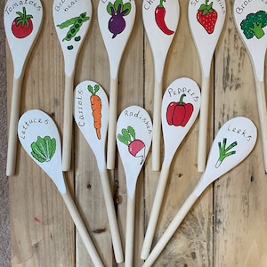 May include: A selection of wooden spoons, each painted white and featuring a different vegetable illustration and name. Vegetables include tomatoes, broad beans, beetroot, chillies, strawberries, broccoli, lettuces, carrots, radishes, peppers, and leeks.