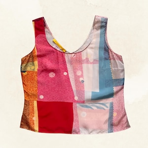 May include: A sleeveless tank top featuring a vibrant patchwork design with blocks of red, pink, orange, and blue. The fabric displays a mix of solid colors, dotted patterns, and geometric shapes, with a scoop neckline and a yellow interior label.