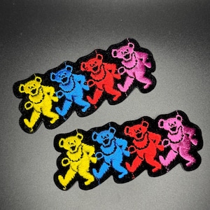 May include: Embroidered patches featuring dancing bears in yellow, blue, red, and pink. Each patch has four bears on a black background. The bears are in a line, with their arms and legs outstretched in a dancing pose.
