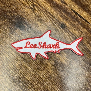 May include: White embroidered shark patch with red outline and the text "Leo Shark" in red.