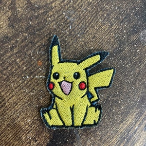 May include: Yellow embroidered patch of Pikachu, a popular cartoon character from the Pokemon franchise. The patch features Pikachu's signature yellow fur, red cheeks, and black eyes.