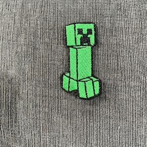 Puede incluir: Parche bordado con el personaje Creeper verde de Minecraft. El parche está hecho de fieltro y tiene un contorno negro.