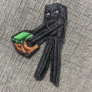 Può includere: Toppa ricamata raffigurante un personaggio di Enderman nero di Minecraft con occhi viola, che tiene in mano un blocco di terra con erba verde e terra arancione. La toppa è realizzata con filo nero e ha un design dettagliato.