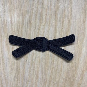 Könnte beinhalten: Eine weiße Keramik-Tasse mit schwarzem Henkel und dem Text "But First, Coffee" in fetter, schwarzer Schrift. Die Tasse steht vor einem verschwommenen Hintergrund, der eine gemütliche Umgebung suggeriert.