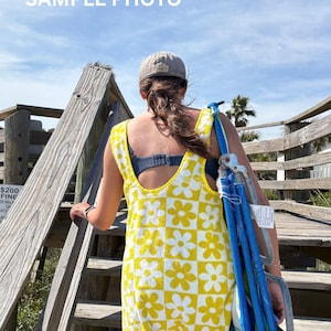 Pode incluir: Um vestido de praia sem mangas com um padrão de xadrez amarelo e branco e um motivo repetido de flores de margarida. A peça tem um decote redondo e alças largas, confeccionada em tecido texturizado com bainha acabada.