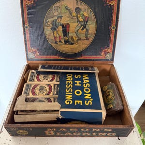May include: Antique wooden shoe blacking box with a hinged lid. The lid features a colorful illustration of two men and boots. Inside are several boxes of shoe dressing and a tin of polish. The box is labeled "MASON'S BLACKING".