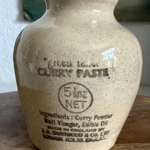 May include: A beige ceramic jar with a speckled finish and a narrow neck. The front features black printed text reading Green Label CURRY PASTE, 5 1/2 oz NET, and a list of ingredients including Curry Powder, Malt Vinegar, and Edible Oil.