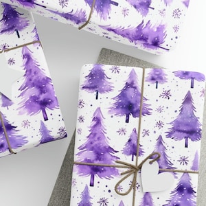 May include: Purple watercolor Christmas tree wrapping paper with a white background and a brown twine bow. The paper is decorated with snowflakes and small purple dots.