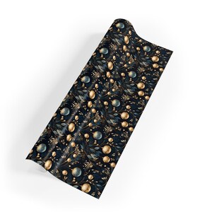 May include: A roll of wrapping paper with a dark blue background and a repeating pattern of gold and teal orbs, leaves, and sprigs. The paper has a glossy finish and is partially unrolled, revealing the design.
