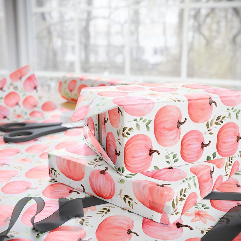 May include: A stack of gift boxes wrapped in white paper with a pink watercolor pumpkin pattern. The boxes are tied with a black ribbon.