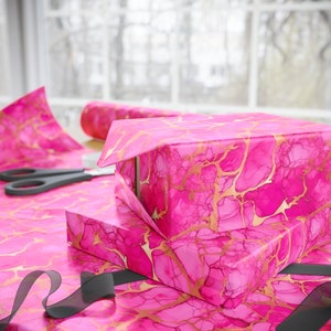 Peut inclure: Papier d'emballage marbr&eacute; rose et or avec un ruban dor&eacute;. Le papier a un motif tourbillonnant et est parfait pour emballer des cadeaux.