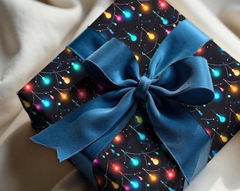 May include: A square gift box wrapped in black paper with a colorful string light pattern. The box is tied with a wide, dark blue satin ribbon and a large bow. The gift is presented on a soft, white fabric.