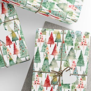 May include: White wrapping paper with a repeating pattern of watercolor Christmas trees in shades of green, red, and pink. The trees are decorated with white dots and have a snowy effect. The paper is tied with twine and a white heart-shaped tag.
