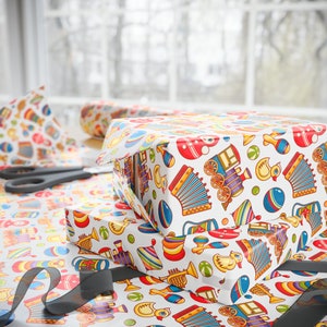 May include: Two gift boxes wrapped in white paper with a colorful pattern of toys, including a train, a duck, a ball, and a musical instrument. The boxes are stacked on top of each other.