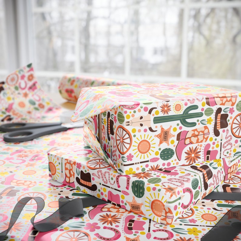 May include: Two gift boxes wrapped in colourful patterned paper with a Western theme. The paper features cacti, horseshoes, stars, and other Western motifs. The boxes are stacked on top of each other.