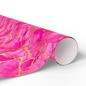 Peut inclure: Papier d'emballage rose avec un motif marbr&eacute; dor&eacute;. Le papier est enroul&eacute; et l'extr&eacute;mit&eacute; est visible.