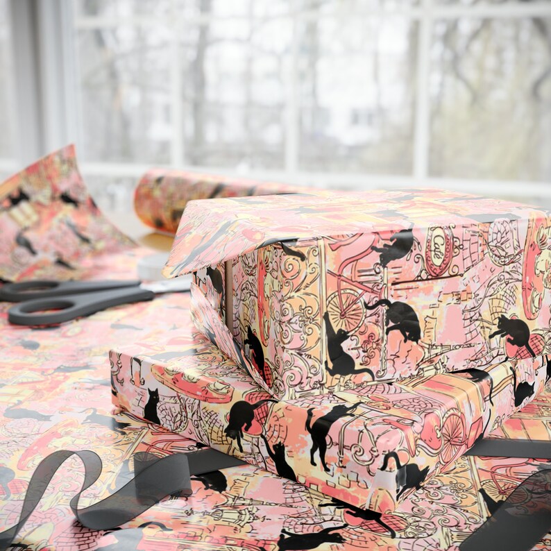 May include: Two gift boxes wrapped in pink and black patterned paper with a black cat design. The boxes are stacked on top of each other and are surrounded by black ribbon.