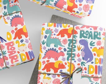 May include: White gift wrap with a colourful dinosaur design, including the words "ROAR" and "DINO". The paper features illustrations of dinosaurs in blue, pink, orange, and yellow. The gifts are tied with twine and a heart-shaped tag, suitable for children.