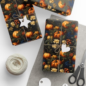 Op de afbeelding: Twee cadeaudozen ingepakt in donkerbruin papier met een patroon van oranje pompoenen, groene bladeren en witte bloemen. De dozen zijn vastgebonden met touw en versierd met witte papieren sterren en harten.