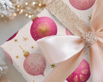 Op de afbeelding: Een cadeau met een kerstthema, verpakt in papier met een patroon van roze kerstballen en gouden sterren. Een lichtroze satijnen strik met een juwelen sluiting en een gouden glitterlint sieren het cadeau.