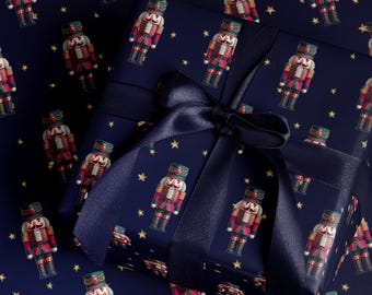 May include: A wrapped gift with navy blue wrapping paper featuring a pattern of toy nutcrackers and gold stars. A navy blue ribbon is tied around the gift. The nutcrackers are red, gold, and blue.
