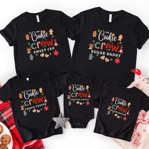 May include: Black t-shirts and a onesie with the text "The Cookie Crew" in a festive design. Each shirt has a different title: Sweet CEO, Sugar Daddy, Cookie Tester, Frosting Fanatic, and Dough Roller. Festive gingerbread men and holiday accents.