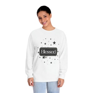 May include: White long-sleeved shirt with a black speech bubble that says "Blessed" and black stars scattered around it.