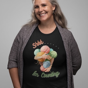 May include: Black t-shirt featuring a graphic of a person holding colourful yarn balls and the text "Shhh... I'm Counting".