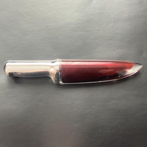May include: A clear, red lip gloss in a silver and clear knife-shaped container.
