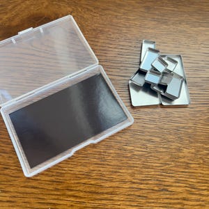 Könnte beinhalten: Ein transparentes Plastikgehäuse mit einem schwarzen magnetischen Einsatz und einem Satz kleiner, silberner Metallbehälter.