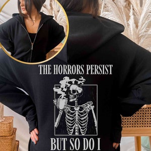 May include: Black hooded sweatshirt with a skeleton holding a cup of coffee and the text "The Horrors Persist But So Do I".