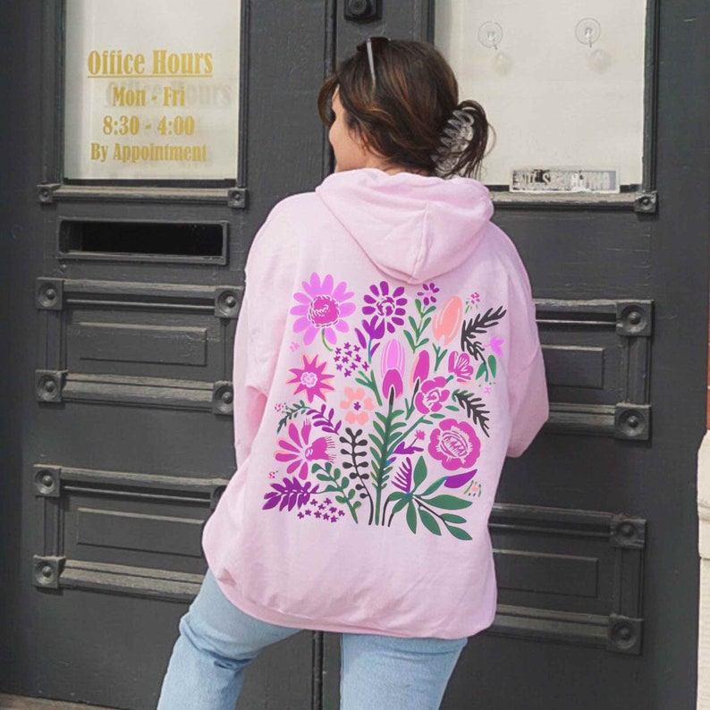 Puede incluir: Sudadera rosa con un dise&ntilde;o floral en la espalda. El dise&ntilde;o presenta flores y hojas rosas, moradas y verdes.