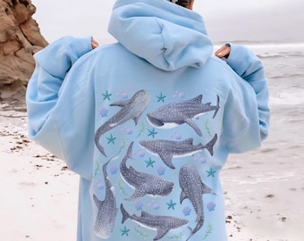 Könnte beinhalten: Ein hellblauer Hoodie mit einem Rückendruck von mehreren Walhaien und Muscheln. Der Hoodie hat eine Kapuze mit Kordelzug.