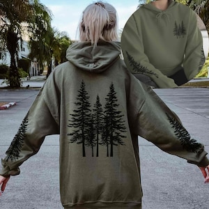 May include: An olive green hoodie with a black tree design on the back and sleeves. The hoodie has a drawstring hood and long sleeves. The design features a group of trees on the back and a tree branch pattern on the sleeves.
