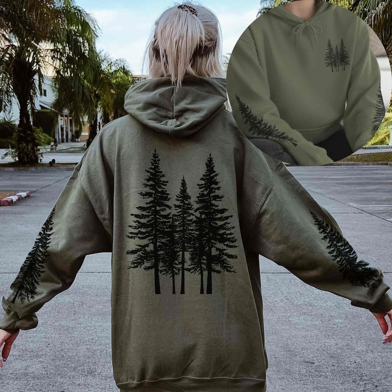 May include: An olive green hoodie with a black tree design on the back and sleeves. The hoodie has a drawstring hood and long sleeves. The design features a group of trees on the back and a tree branch pattern on the sleeves.