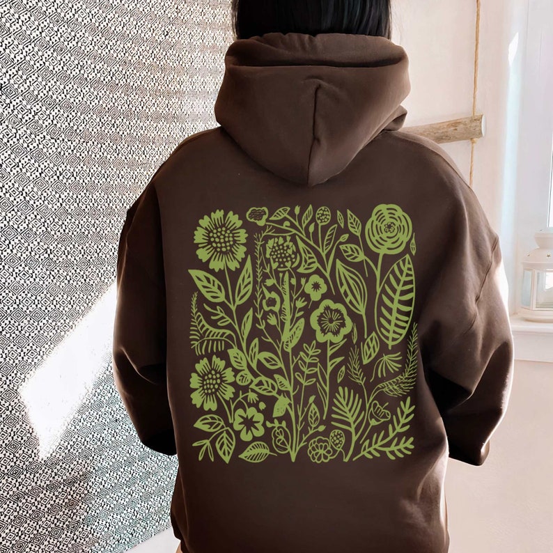 May include: A brown hoodie with a green floral design on the back. The design features a variety of flowers, leaves, and stems.
