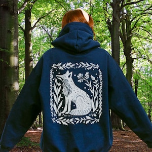 May include: A navy blue hooded sweatshirt with a white graphic of a fox sitting in a floral frame. The fox is looking to the left and has a spotted pattern.