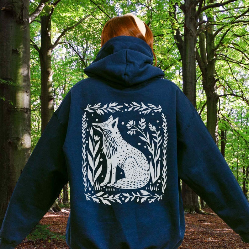 May include: A navy blue hooded sweatshirt with a white graphic of a fox sitting in a floral frame. The fox is looking to the left and has a spotted pattern.