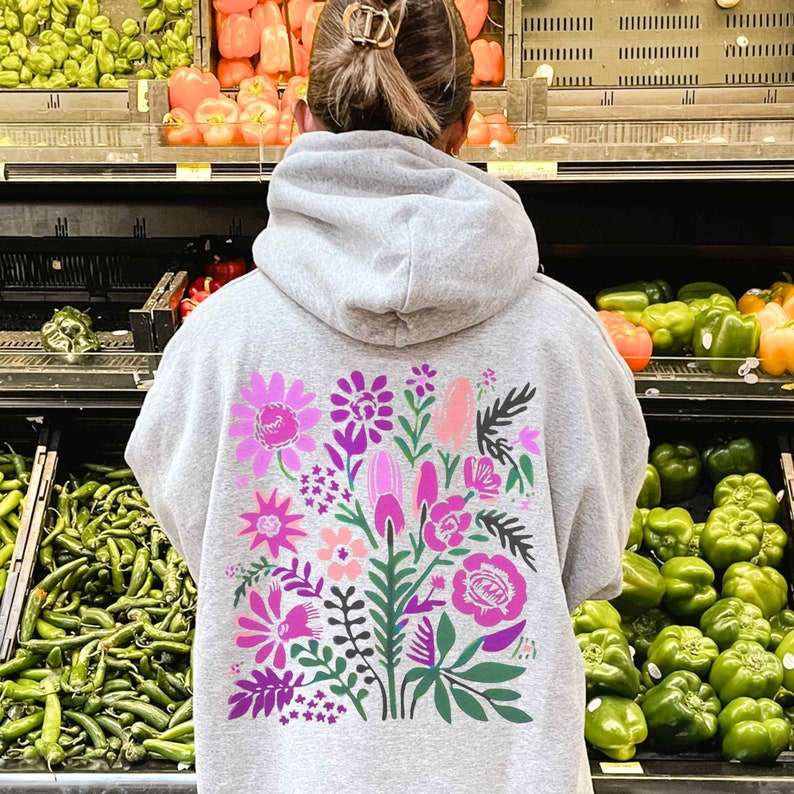 Puede incluir: Una sudadera con capucha gris con un estampado floral en la espalda. El estampado presenta flores y hojas rosas, moradas y verdes.